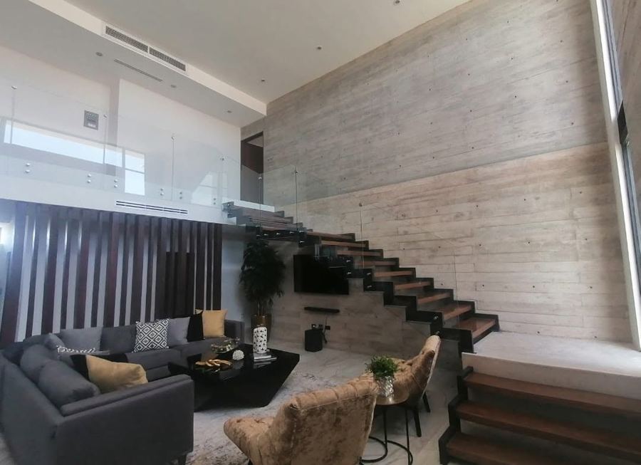 Sala en doble altura con escalera flotante y muro de concreto aparente