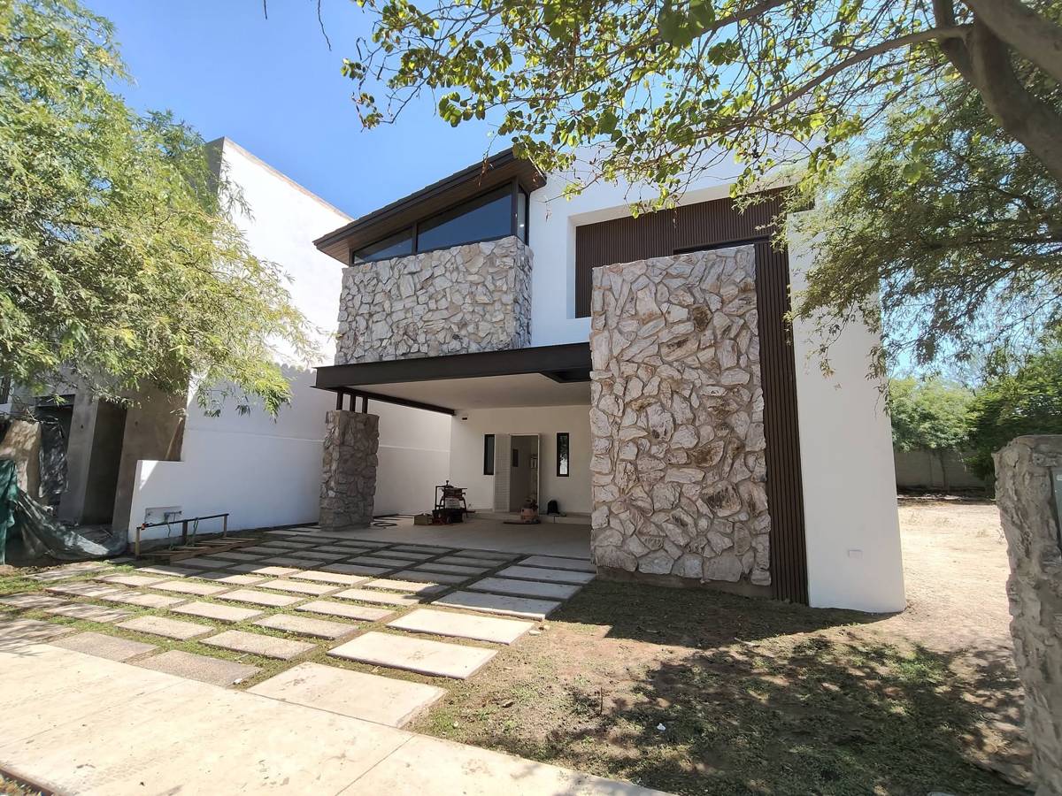 Fachada de casa de dos plantas con muros de piedra y cochera